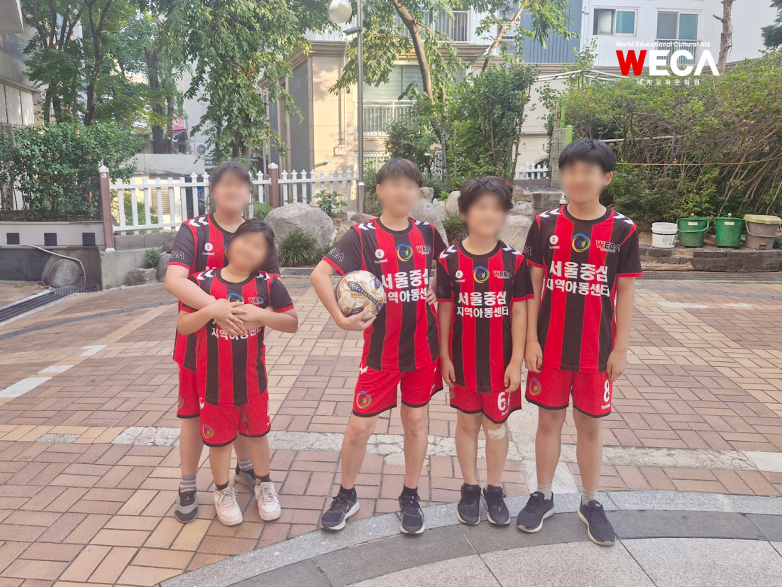 위카 유니폼을 맞춰입고 축구공을 들고 기념사진을 찍는 지역아동센터 아동들