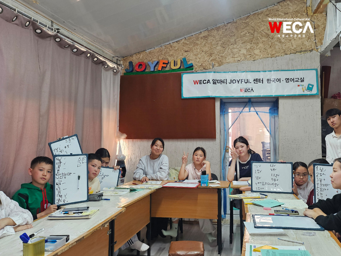 한글로 또박또박 받아쓰기를 한 작은 화이트보드를 저마다 자랑스럽게 들어 보이며 카메라를 보고 활짝 웃는 아이들