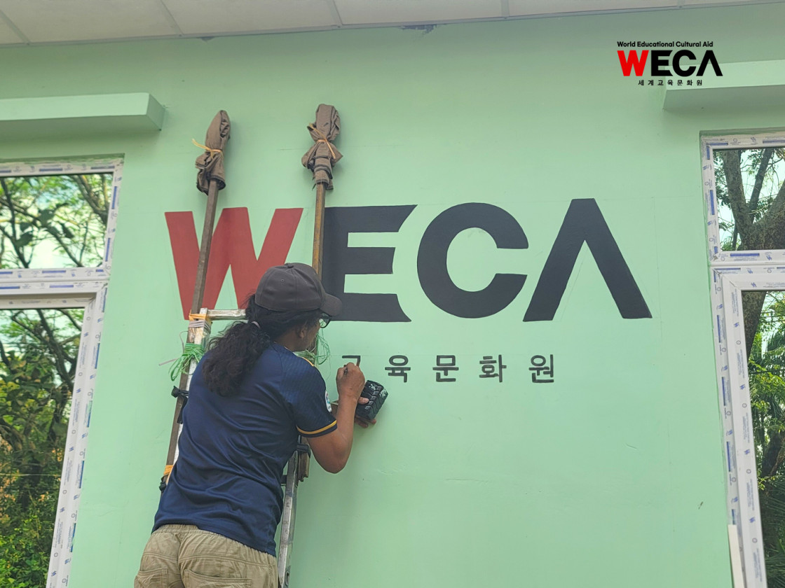 미얀마 쉐비다 17번학교 신축 교실 외벽에 세계교육문화원 WECA 로고와 문구를 정성스럽게 그리고 완성해 나가는 모습